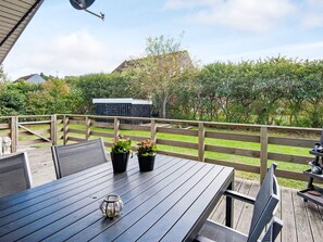 An outdoor deck with a wooden table and chairs, potted plants, and a clear view of the surrounding garden and trees.
