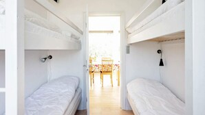 Una habitación estrecha con dos literas, suelo de madera y una puerta que da a un comedor con una mesa y sillas.