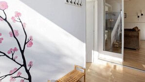Un interior moderno con un banco de madera, una pared blanca con un mural de flores de cerezo y una puerta de cristal que da a otra habitación.