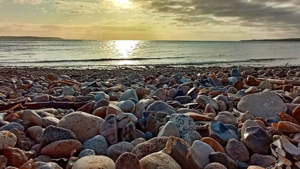 Una playa rocosa con un atardecer sobre el agua.