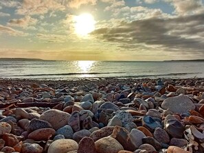 En stenstrand med en solnedgång i bakgrunden.