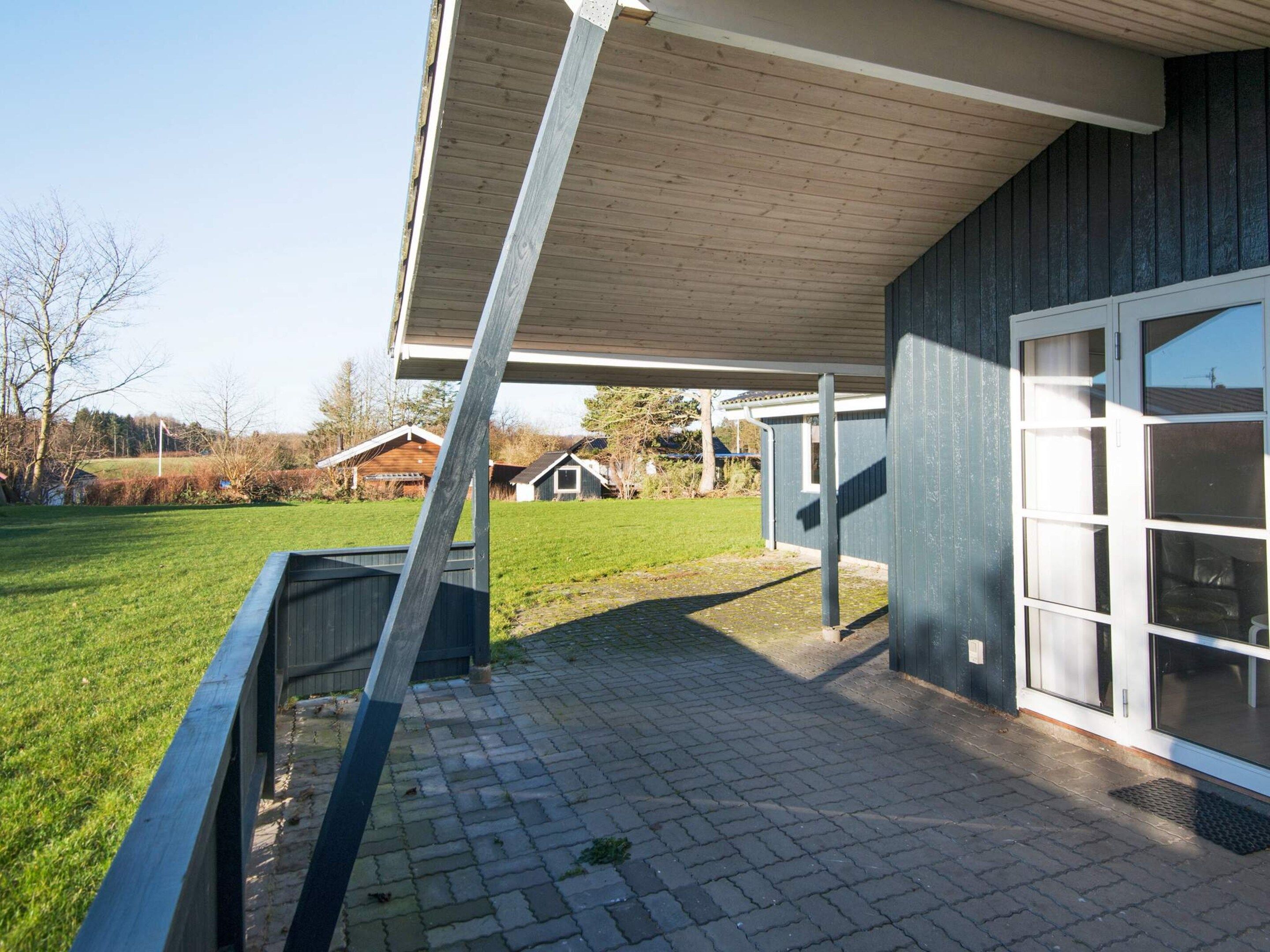 A covered outdoor area with a brick floor, a wooden deck, and a building with a large window.
