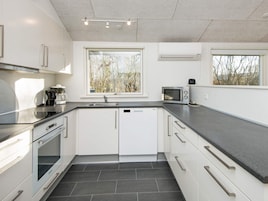 A modern kitchen with white cabinets, a black countertop, a built-in oven, and a window with a view of trees.