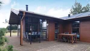 A modern house with a wooden deck, a dining area with a table and chairs, and large windows.