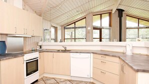 A kitchen with wooden cabinets, a stove, a dishwasher, and large windows with blinds.