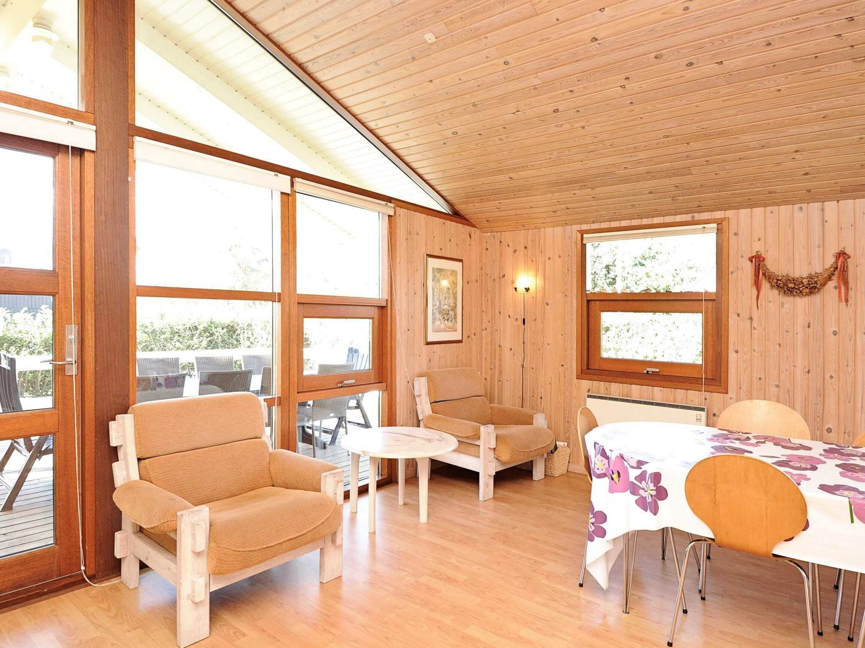 A wooden-paneled room with a sofa, chairs, a table, and large windows.