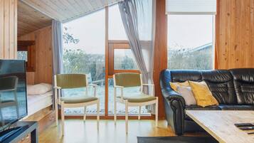 A cozy living room with a television, two chairs, a sofa, and a large window.