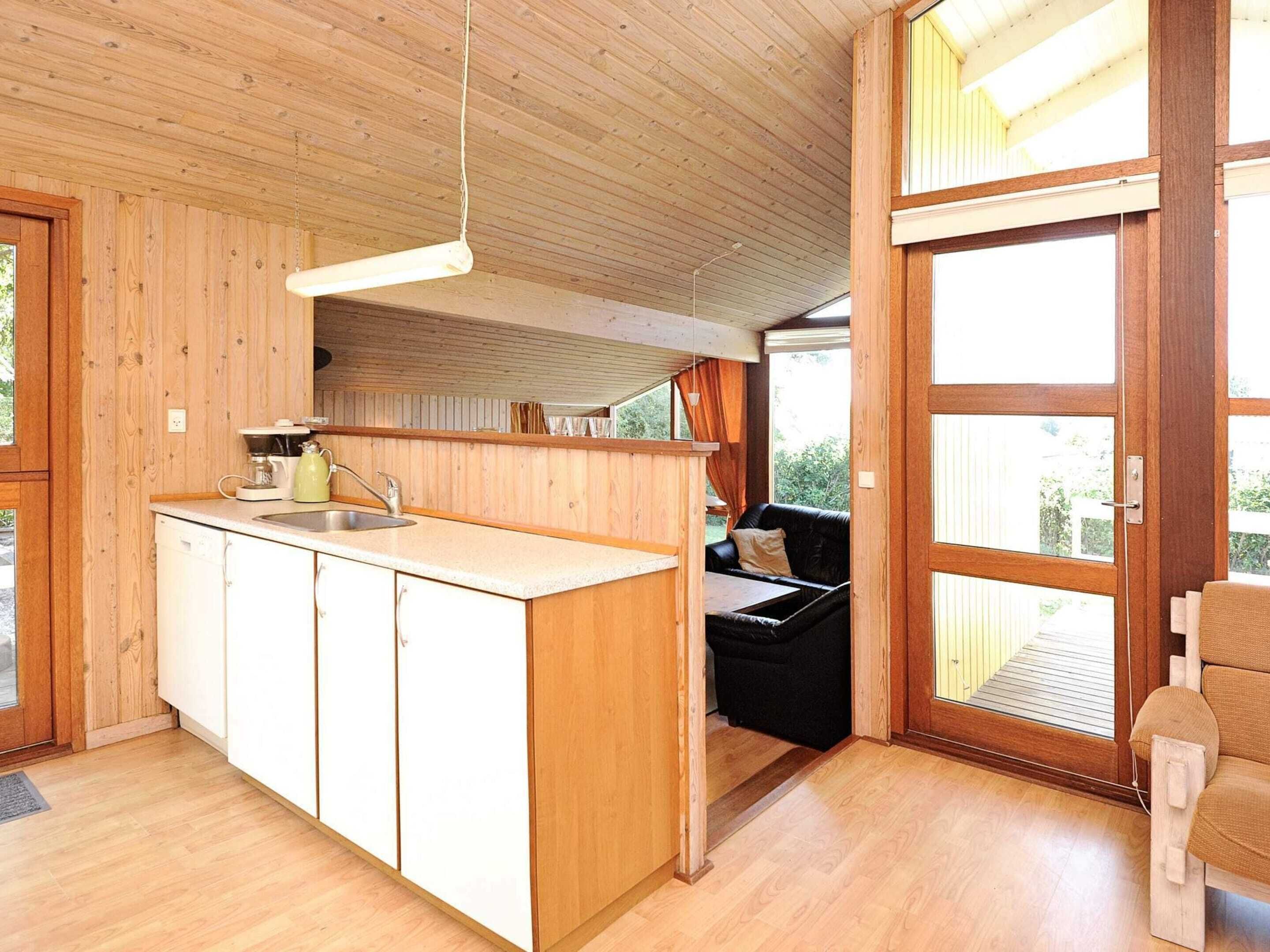 A compact kitchen with wooden cabinets, a sink, and a dining area with a black sofa and a wooden chair.