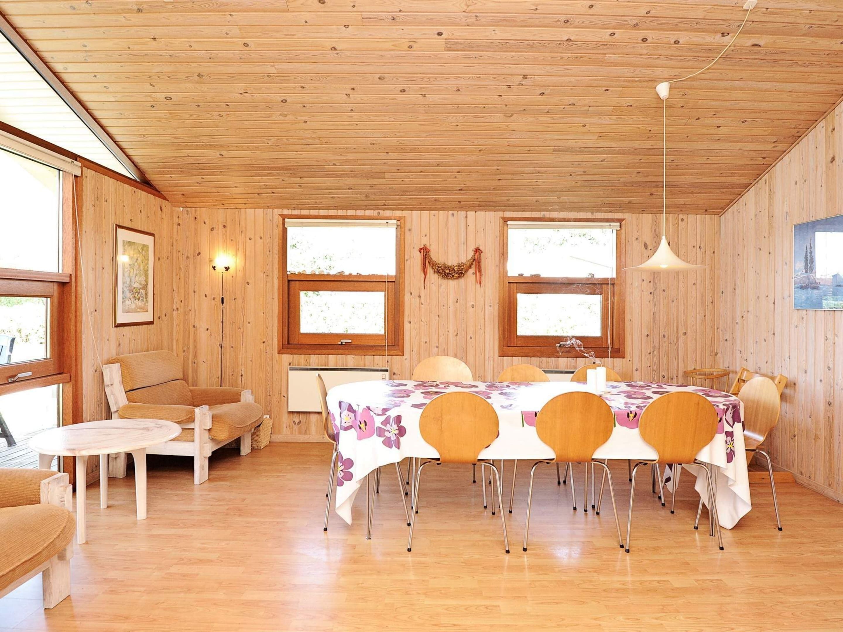 Una habitación con paneles de madera, con una mesa de comedor dispuesta para seis personas, rodeada de sillas. Hay un sofá y una pequeña mesa redonda en la esquina.