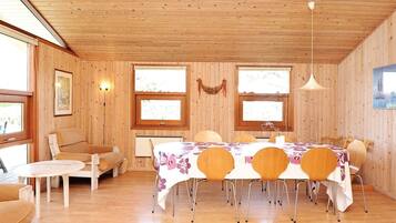 A wooden-paneled room with a dining table set for six, surrounded by chairs. There is a sofa and a small round table in the corner.