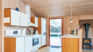 A modern kitchen with wooden cabinets, a built-in oven, a microwave, and a wood-burning stove. - 4 Star Holiday Home in Juelsminde (Horsens)