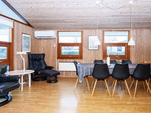 A wooden-paneled room with a dining table, chairs, a black leather chair, a small table with a lamp, and framed pictures on the walls. - 4 Star Holiday Home in Juelsminde (Horsens)