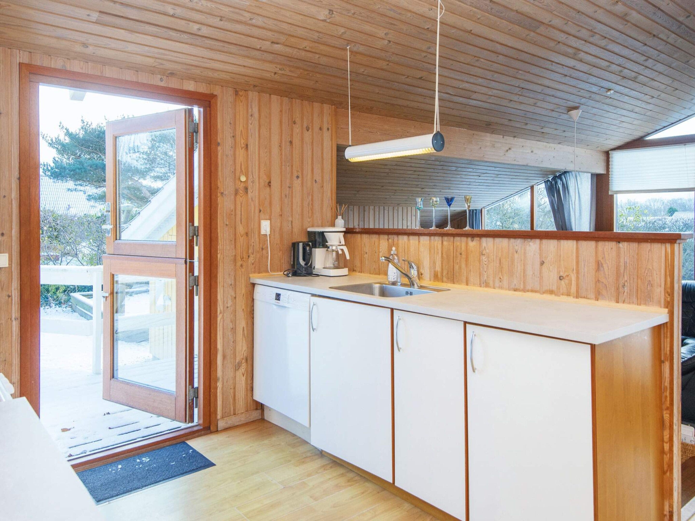 A kitchen with a wooden interior, a built-in dishwasher, a sink, and a hanging light fixture.