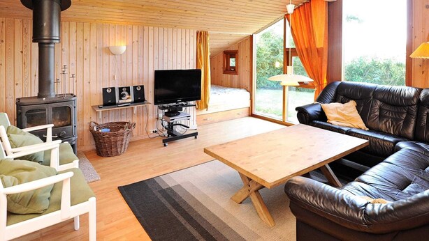 A cozy cabin interior with a wood-burning stove, a television, a leather sofa, and a dining table. - 4 Star Holiday Home in Juelsminde (Horsens)