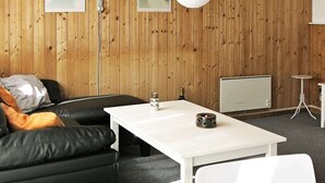 Una stanza con parete rivestita in legno, un divano in pelle nera, un tavolo bianco e un termosifone bianco.