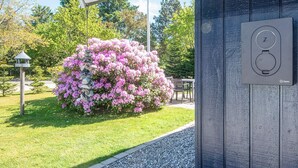 A garden with pink flowers, a stone wall, and a table under a canopy. - Captivating Holiday Home in Ulfborg near Sea (Ulfborg)
