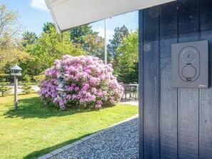 A garden with pink flowers, a stone wall, and a table under a canopy. - Captivating Holiday Home in Ulfborg near Sea (Ulfborg)