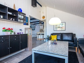 A modern living room with a black leather sofa, a coffee table, and a kitchen area in the background. - Captivating Holiday Home in Ulfborg near Sea (Ulfborg)