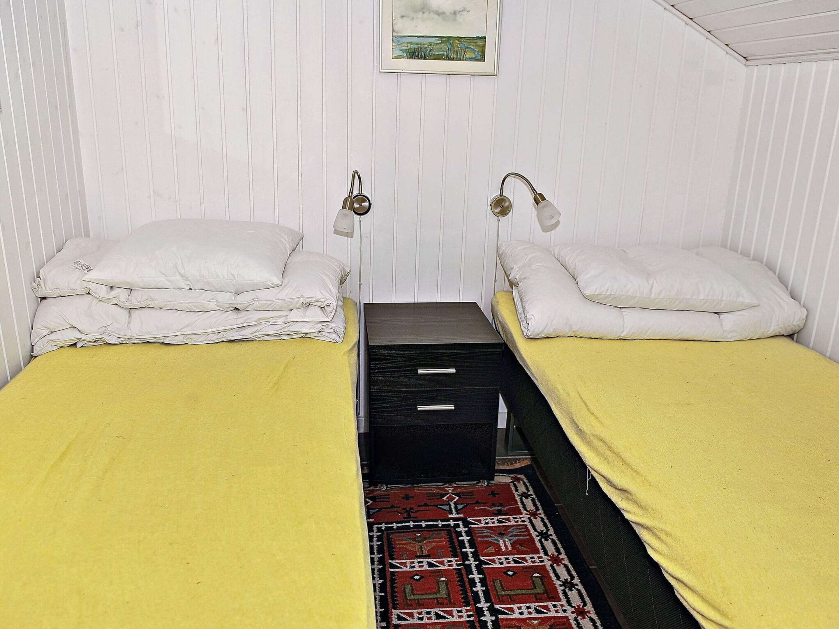 A small, single-room accommodation with two single beds, a black storage unit, a patterned rug, and a framed picture on the wall.