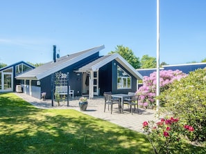 A modern house with a sloped roof, a patio with outdoor furniture, and a garden with flowering plants. - Captivating Holiday Home in Ulfborg near Sea (Ulfborg)