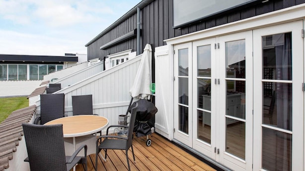 Eine Terrasse mit Tisch, Stühlen, einem Grill und einer Schiebetür zu einem überdachten Bereich.