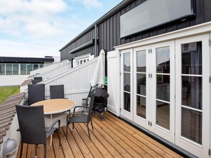 Eine Terrasse mit Tisch, Stühlen, einem Grill und einer Schiebetür zu einem überdachten Bereich.