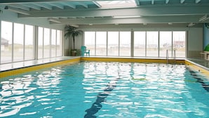 Ein Hallenbad mit klaren Fenstern, einer Palme und einem grünen Stuhl.