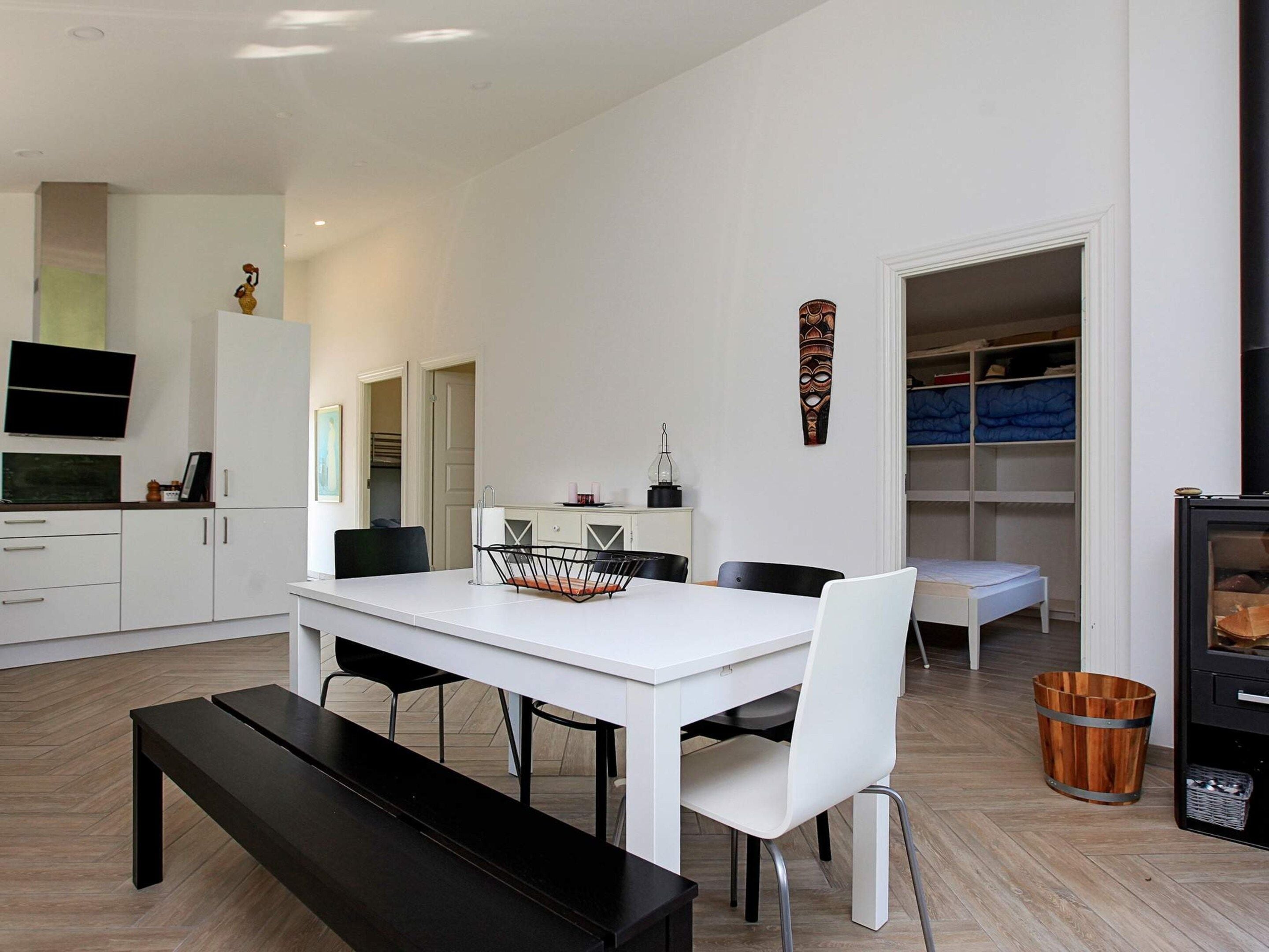 A modern kitchen with white cabinetry, a dining table with chairs, a bench, and a television mounted on the wall.