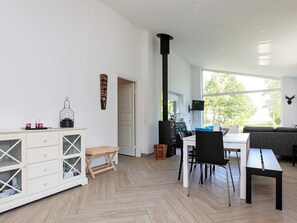 A modern interior with a dining area, a fireplace, and a large window offering a view of the outdoors. - Woodland Holiday Home in Jægerspris with Hot Tub (Jægerspris)
