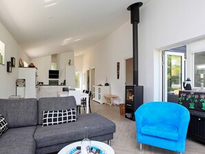 A modern living room with a sofa, a blue armchair, and a fireplace. - Woodland Holiday Home in Jægerspris with Hot Tub (Jægerspris)