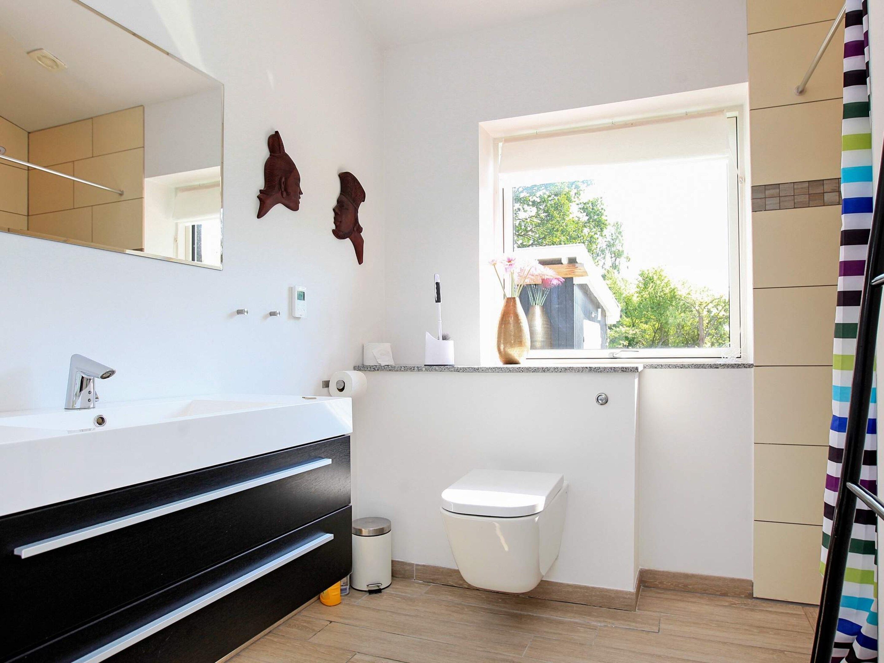 Une salle de bain moderne avec un lavabo blanc, un meuble-lavabo noir et des toilettes. Une fenêtre laisse entrer la lumière naturelle et offre une vue sur la verdure à l’extérieur.