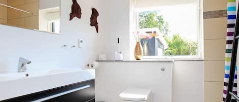 A modern bathroom with a white sink, black vanity, and a toilet. There is a window providing natural light and a view of greenery outside.