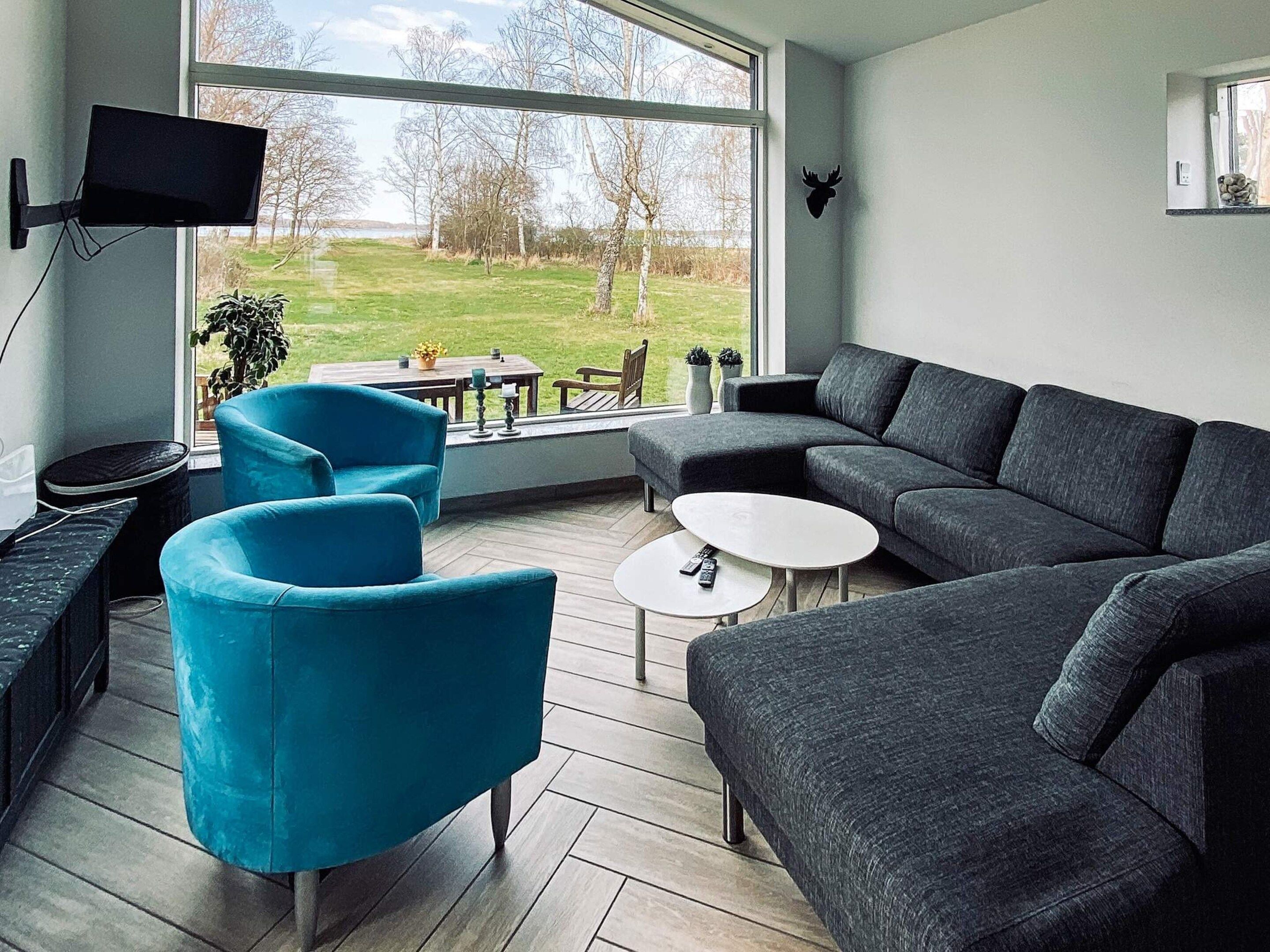 A modern living room with a sectional sofa, two armchairs, a coffee table, and a flat-screen TV mounted on the wall.
