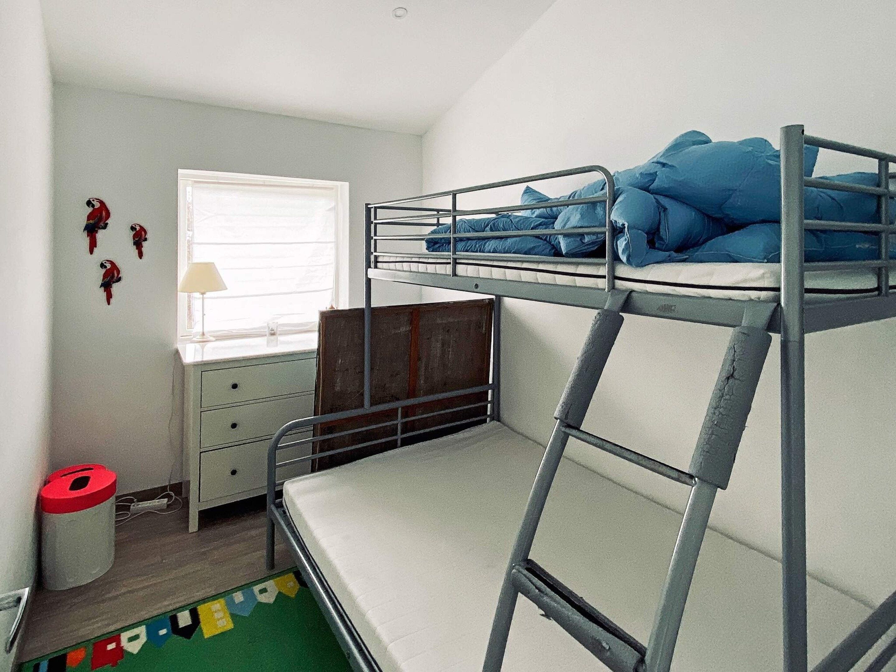 A bunk bed room with a window, a desk, and a trash bin.