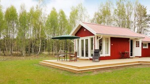 Ett rött trähus med en inglasad uteplats, inklusive ett bord och stolar, och ett grönt parasoll.