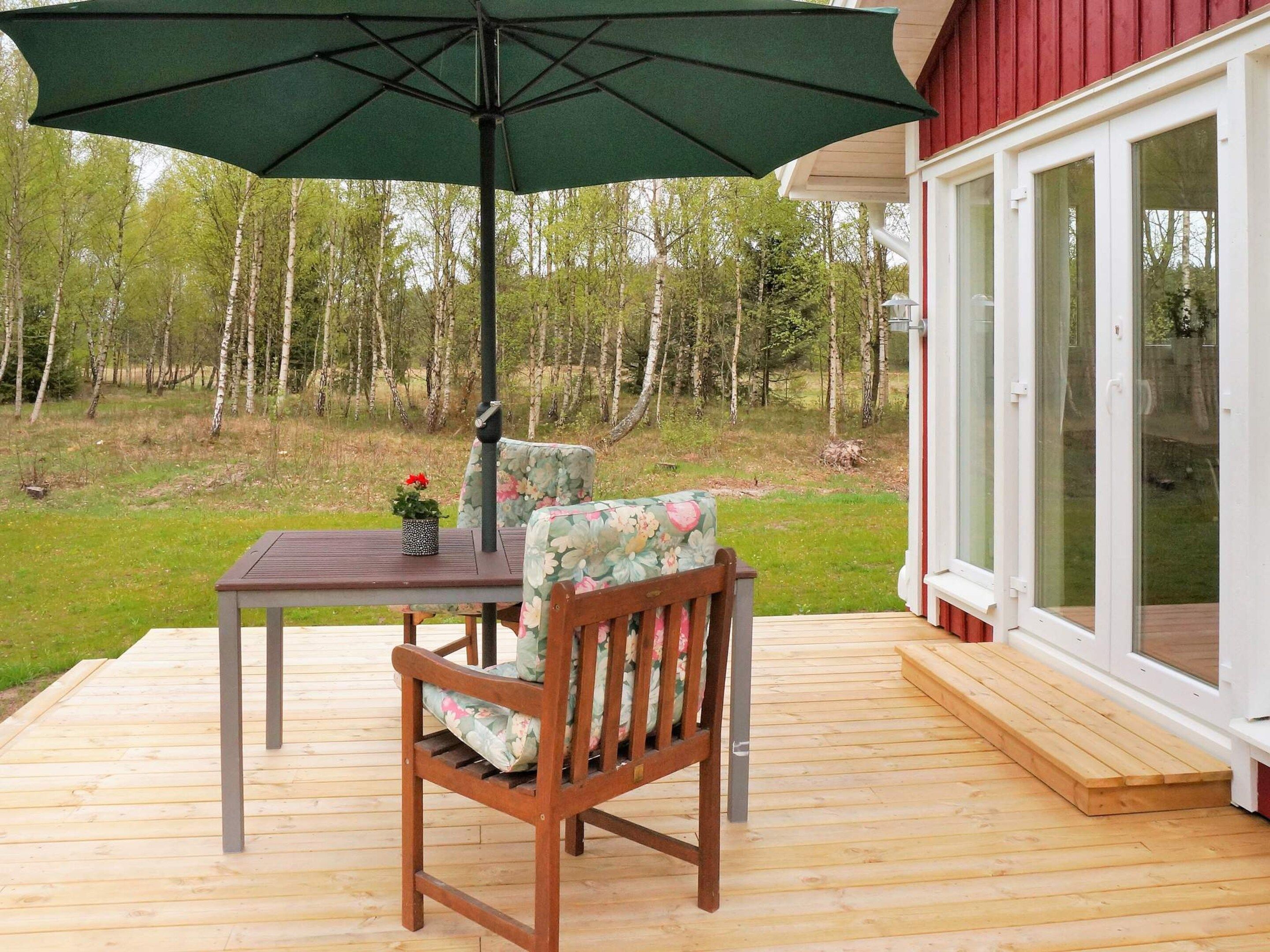 A wooden deck with a table and chairs, an umbrella, and a glass door leading to a wooded area.