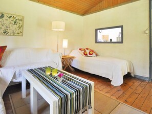 A room with two beds, a small table with a striped tablecloth, a lamp, and a framed picture on the wall.