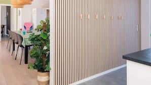 A modern interior with a wooden slat wall, a dining area with chairs and a table, and a hanging rattan light fixture. - 4 Star Holiday Home in Glesborg (Glesborg)