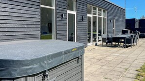 A modern building with large windows, a patio area with outdoor seating, and a hot tub. - 4 Star Holiday Home in Glesborg (Glesborg)