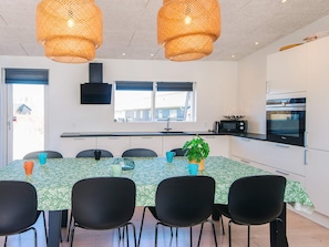 A modern kitchen with a built-in oven and microwave, a dining table with chairs, and a large window providing natural light. - 4 Star Holiday Home in Glesborg (Glesborg)