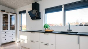 A modern kitchen with white cabinets, a black countertop, and a window with blinds. - 4 Star Holiday Home in Glesborg (Glesborg)