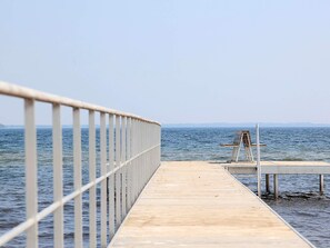 A wooden pier extending into calm waters with a metal railing on one side and a wooden bench on the other.