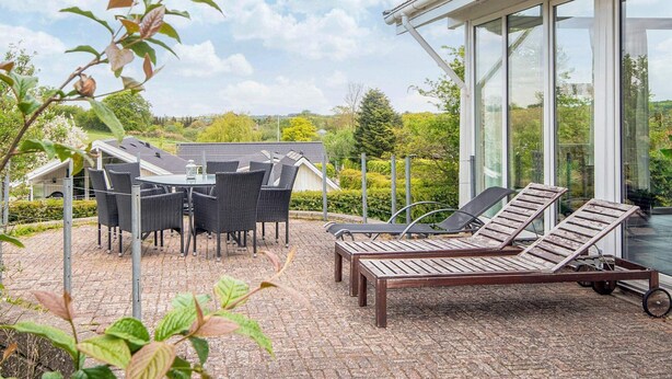 A patio with outdoor furniture, a glass-enclosed room, and a view of the surrounding landscape.
