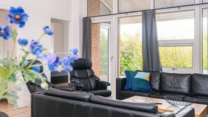 A modern living room with a black leather sofa, a black leather chair, and a wooden coffee table. There is a large window with a view of greenery outside.