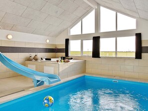 An indoor swimming pool with a blue slide, a reception desk, and large windows.