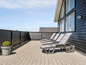 A rooftop patio with lounge chairs and a potted plant.