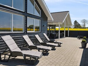 A covered outdoor seating area with lounge chairs and a patio table, adjacent to a building with large windows. - 5 Star Holiday Home in Bogense (Bogense)