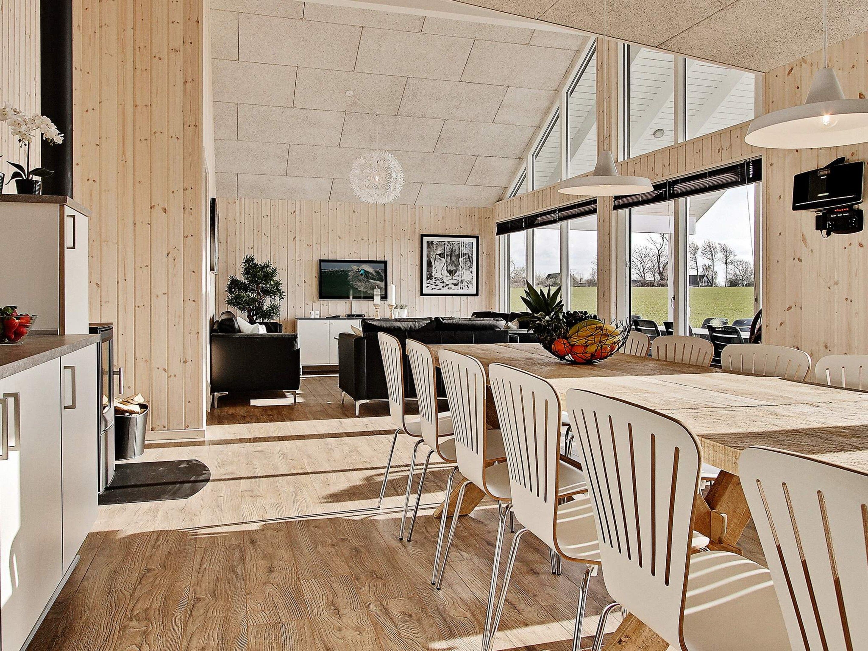 A modern kitchen with a dining area, wooden walls, and large windows.