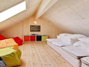 A loft bedroom with a sloped ceiling, wooden walls, a bed, a TV, and a storage unit.