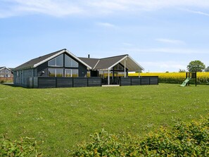 A modern house with a large lawn, a covered patio, and a playground.